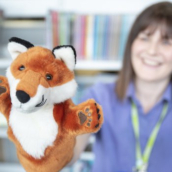 Female member of staff running a rattle, rhyme and roll session in the library, holding up a fox hand puppet.