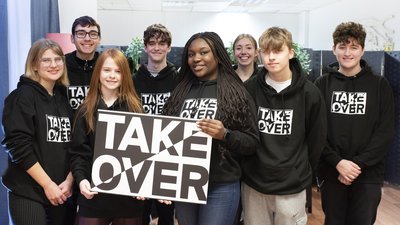 Takeover students wearing Takeover hoodies and holding banner