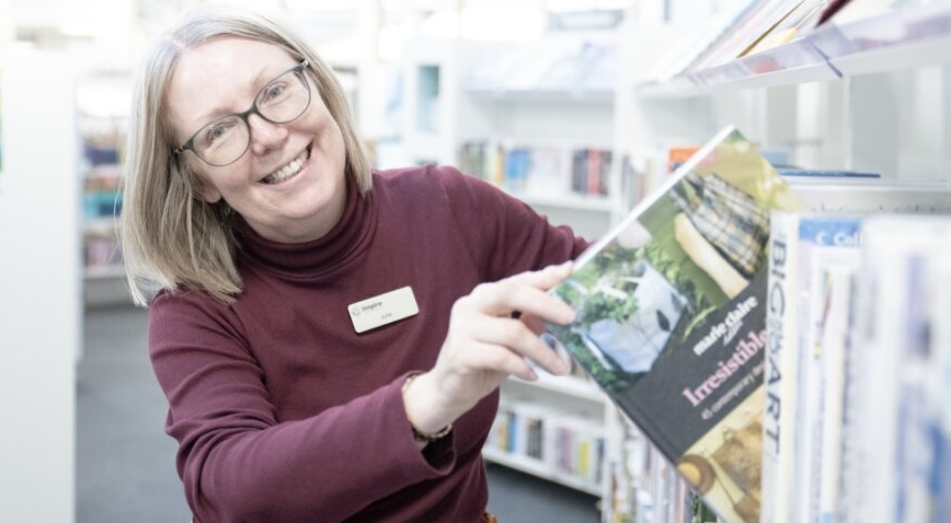 A member of staff at Mansfield Woodhouse library shelving books and smiling