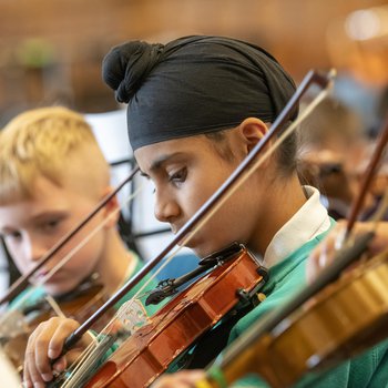 A boy in a turquoise jumper plays the violin