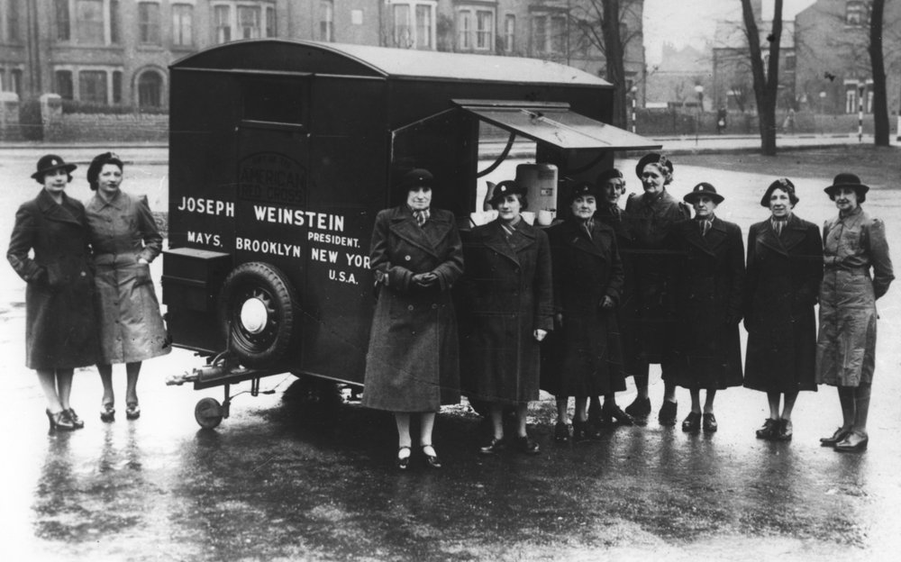 Black and White Image of women in coats and hats stood in front of a trailer.