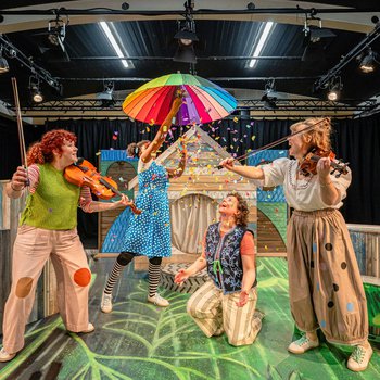 Ruby opens a rainbow umbrella, sending scraps of coloured paper raining onto the three musicians