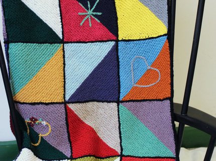 A colourful knitted blanket stitched out of squares on a black chair