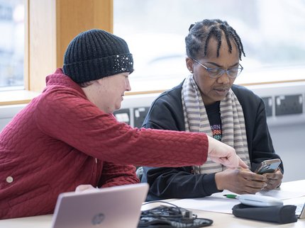 Two learners at laptops talk to each other about their course.