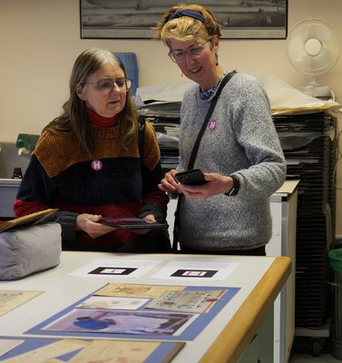 Two female visitors looking at a smartphone. In front of them is a display of archive documents.