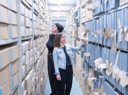 Two people walking between shelves at Nottinghamshire Archives, fascinated at the documents beside them