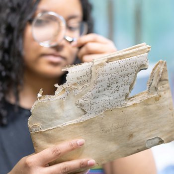 Conservator looking at a damaged document with a magnifying glass