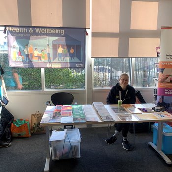 Person sat behind a stall with leaflets, beside another person stood up