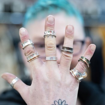 Photo of artists hand showcasing several rings on their fingers.