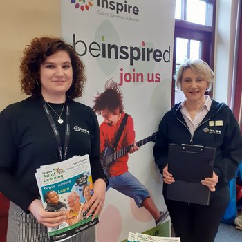 Two people working for Inspire at our stall. They are holding our leaflets.