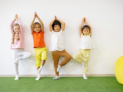 Four children standing in yoga pose with arms raised above their heads.