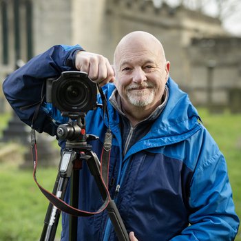 Photo of man next to his camera stood in front of a church.