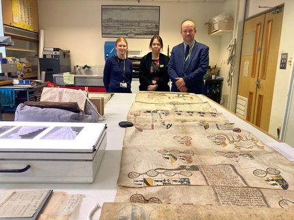 1 man and two women stood behind a table that has various heritage objects on at the Nottinghamshire Archives