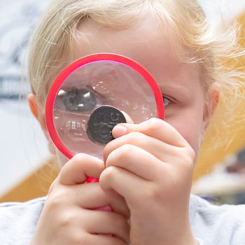 A girl looking at an old coin through a magnifying glass.