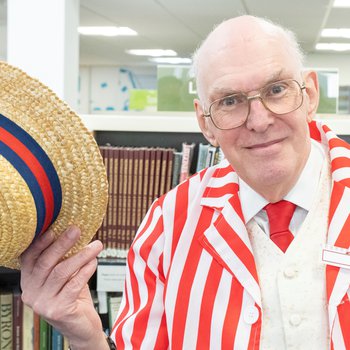 A man dressed up in 1920s clothing including a red and white striped blazer red tie and straw hat.