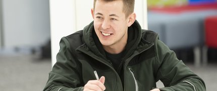 A smiling young man holding a pen