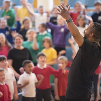 A man opens his arms and sings with children in the background