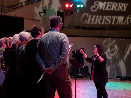 A choir performs with lights in the background reading "merry christmas"