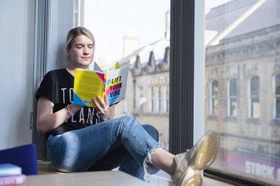 Blonde woman sitting by a window reading a book
