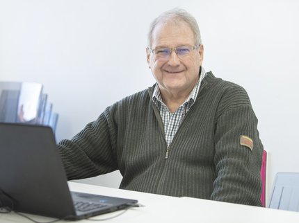 A white man with grey hair wearing glasses and smiling sits at a desk with a laptop ready to learn.