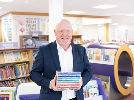 Man in suit holding a stack of books in a colourful children's library