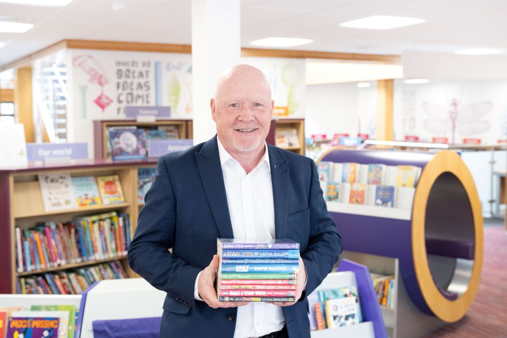 Man in suit holding a stack of books in a colourful children's library