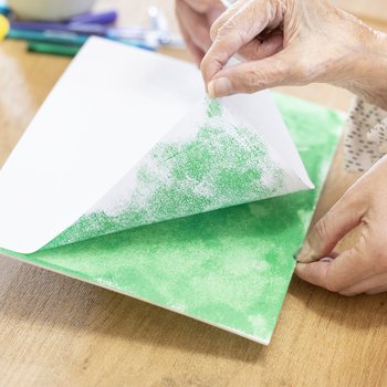 Photograph of care home resident peeling back an inked sheet of paper to reveal the green design