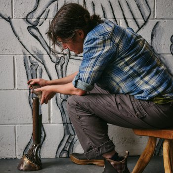 Photo of sculptor Michelle sat in front of a wall mural of prehistoric horse