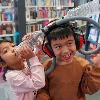 Two children playfully experiment with sound using a headset device.