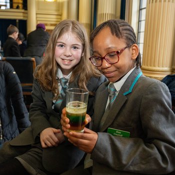 Two secondary school students hold a beaker containing liquid.