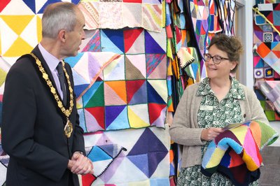 A woman smiles and holds a knitted blanket while talking to a man