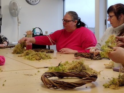 A group of people around a table adding moss to willow wreaths