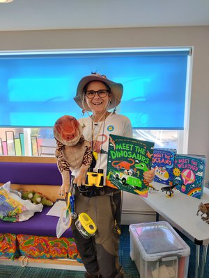 Author Caryl Hart smiling with a puppet and a copy of her book, Meet the Dinosaurs