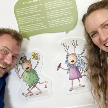 Selfy photograph of Amanda Rigby and Mark Grist stood in front of a poem and monster they created for the Expression Exhibition