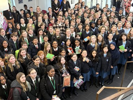 A group of around 200 school pupils holding books and smiling