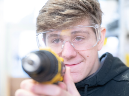 A young man holding an electric drill and looking towards the camera