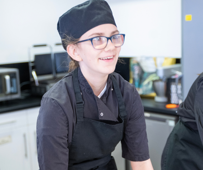 A catering student in chef uniform smiles at the camera