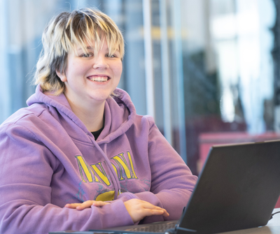 An Inspire College learner in a purple hoodie with a laptop