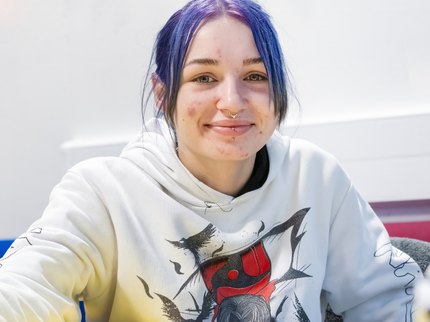 A young Inspire College student with purple hair in a ponytail is smiling at the camera