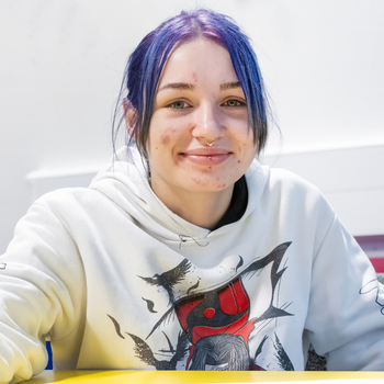 A young student with her purple hair tied back in a ponytail is smiling at the camera