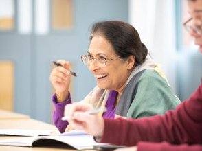 A learner smiles at their desk and holds a pen