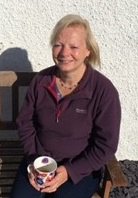 New Board member Jackie Hewlett-Davies sitting on a bench holding a cup of tea