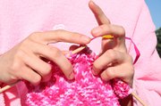 hands knitting a pink and white scarf