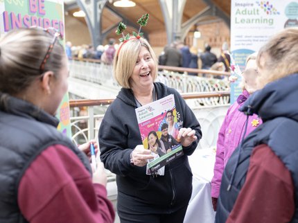 An Inspire staff member wearing a Christmas headband, holding a course guide and speaking to customers.