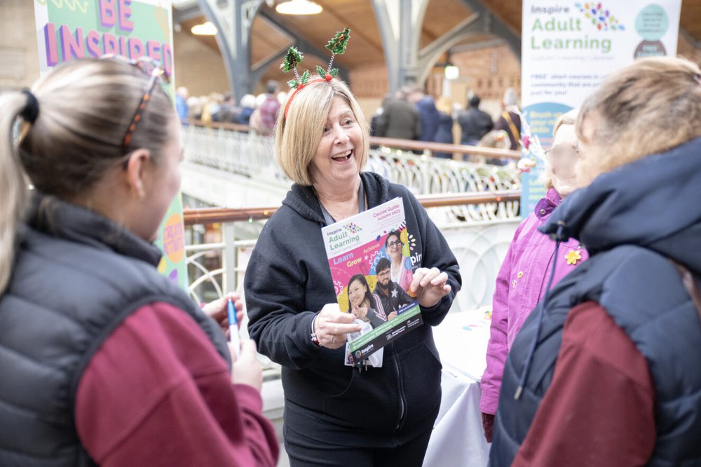 An Inspire staff member wearing a Christmas headband, holding a course guide and speaking to customers.