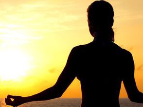 A woman sits and meditates in front of a sunset