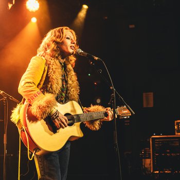 A person with long curly hair playing guitar and signing on stage