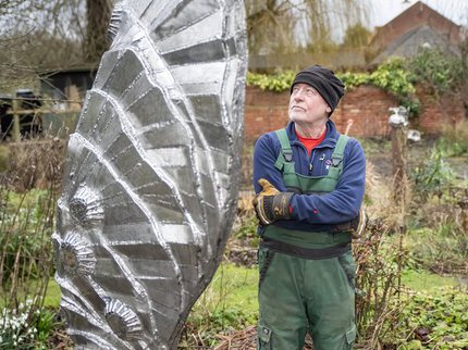 A man stands outside next to a metal sculpture of a wing