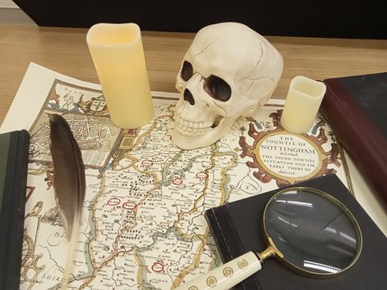 Desk with map, magnifying glass, candles, quill pen, books and skull