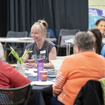 A woman in a grey top smiling and sitting a table